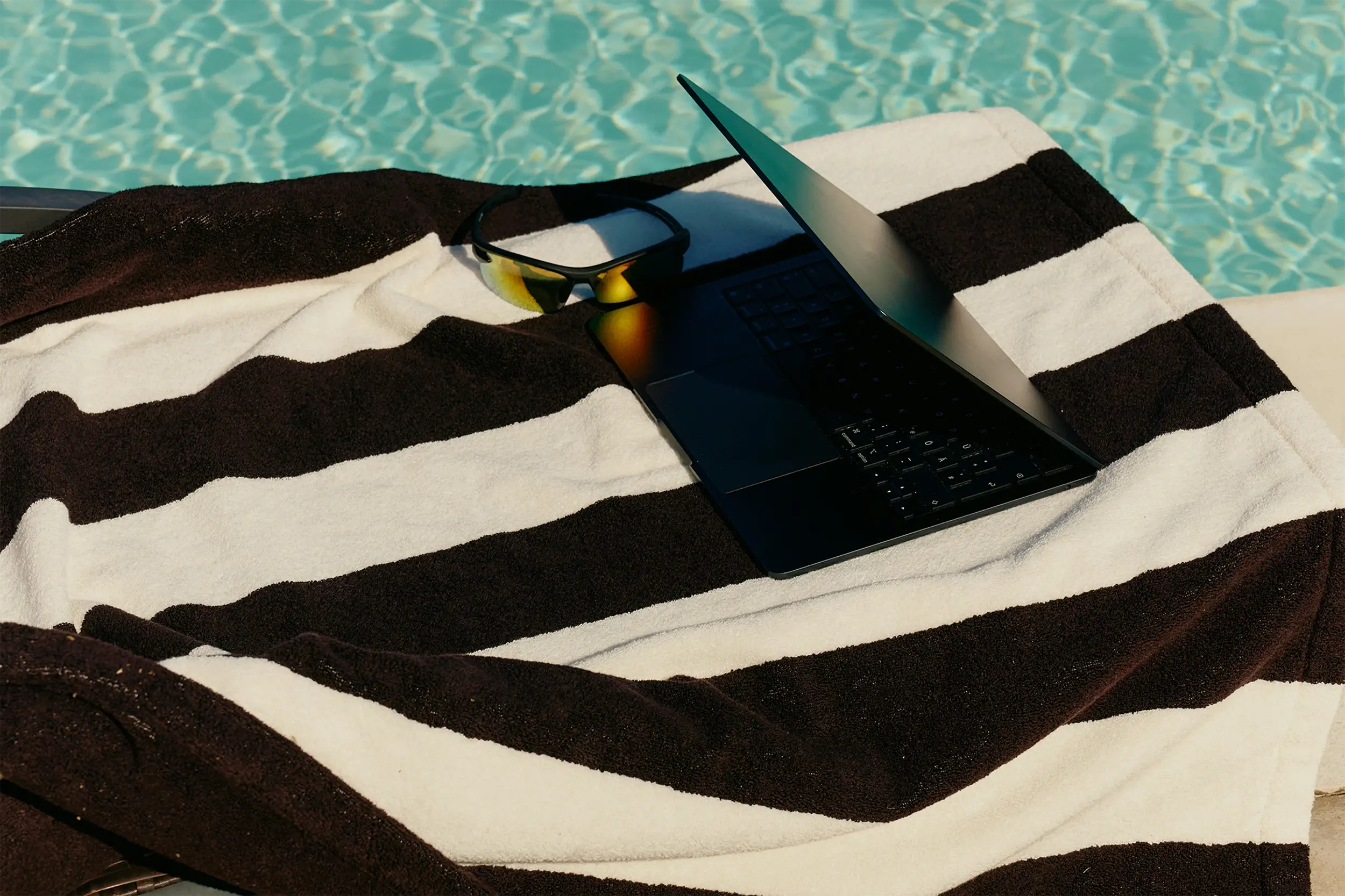 laptop on top of a beach towel by the pool