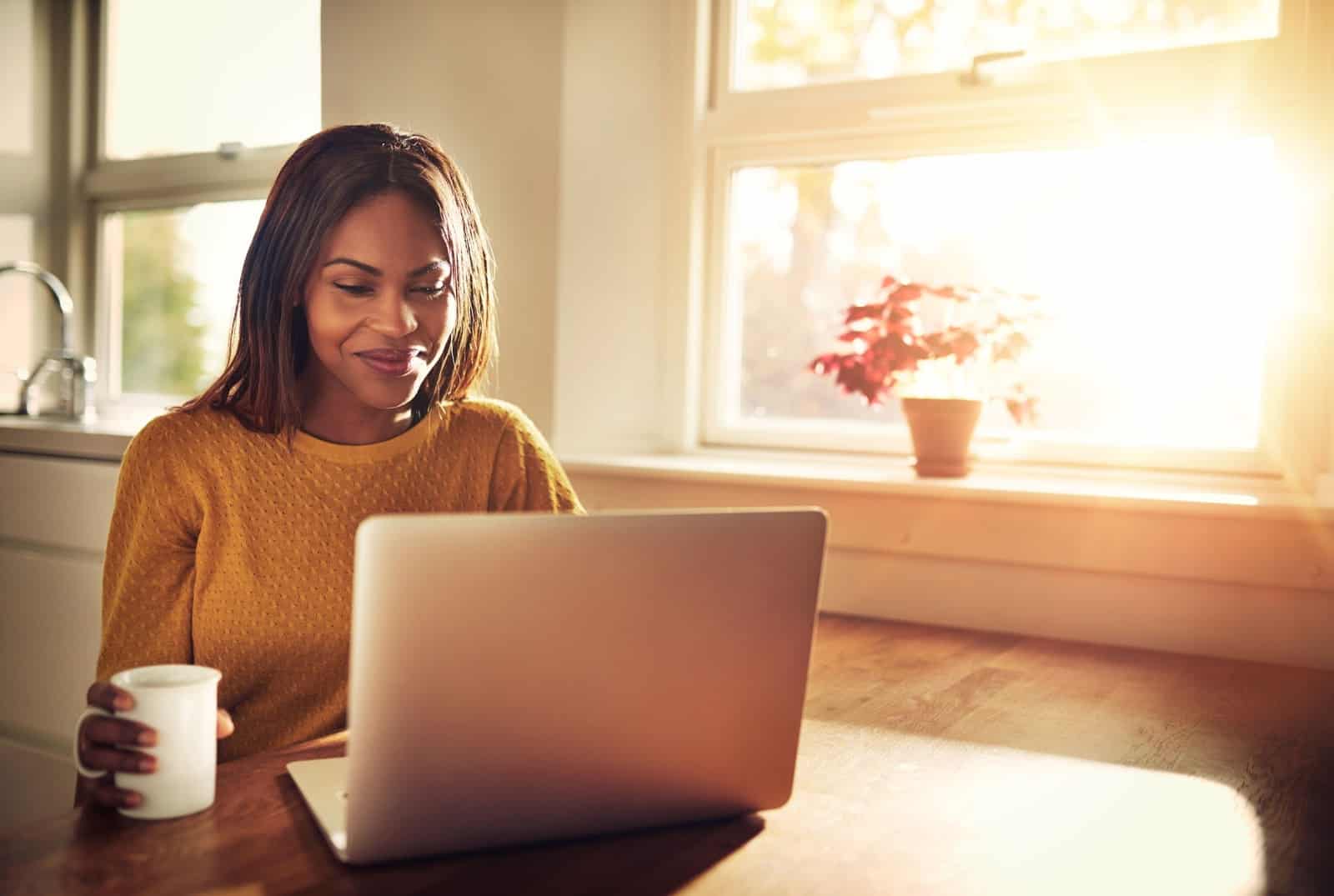 woman with mug at a table in front of a laptop