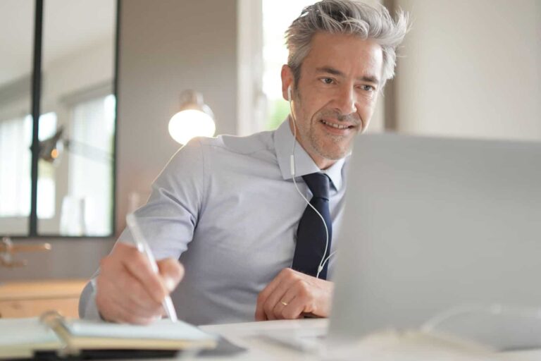 man sitting at desk with pen in front of laptop