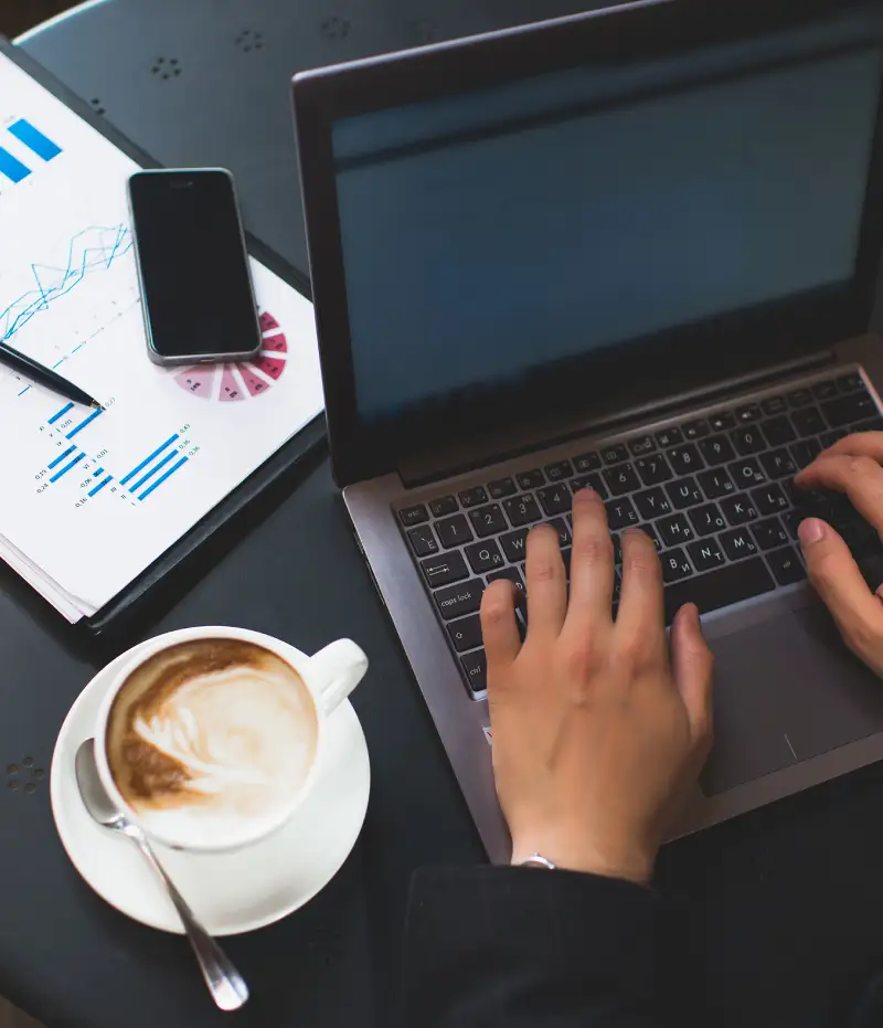 person typing at table with coffee and graphs