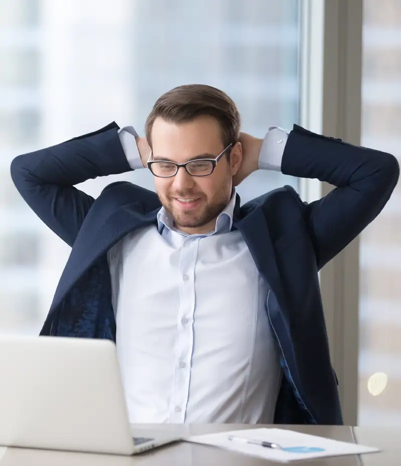 man crossing his hands behind his head looking at a laptop