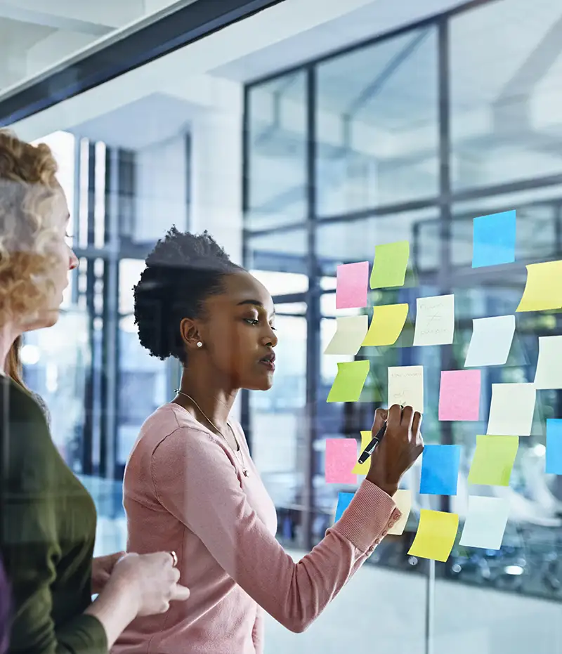 woman writing on note cards stuck to a glass wall
