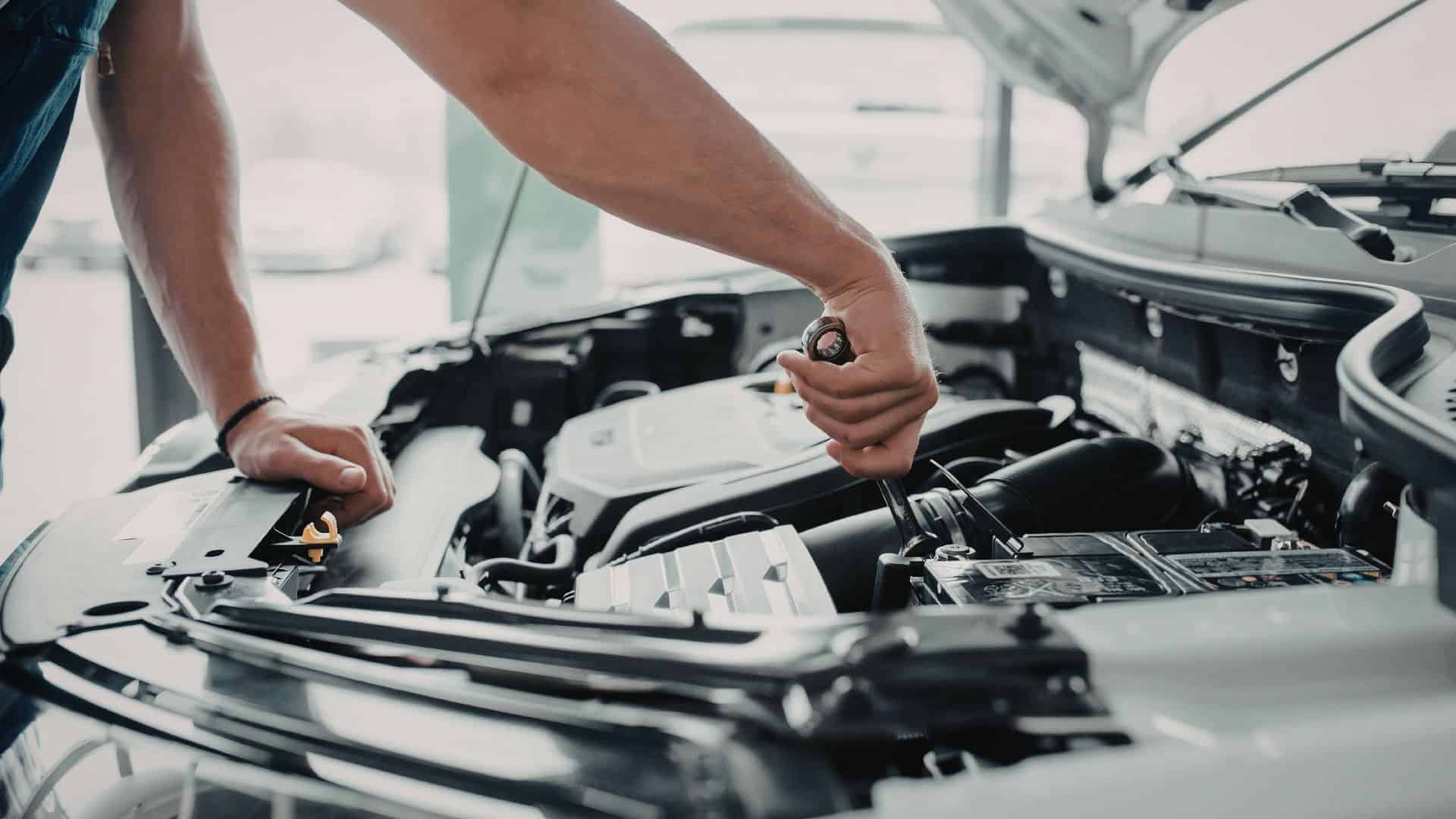 person working on a car with the hood open holding a wrench